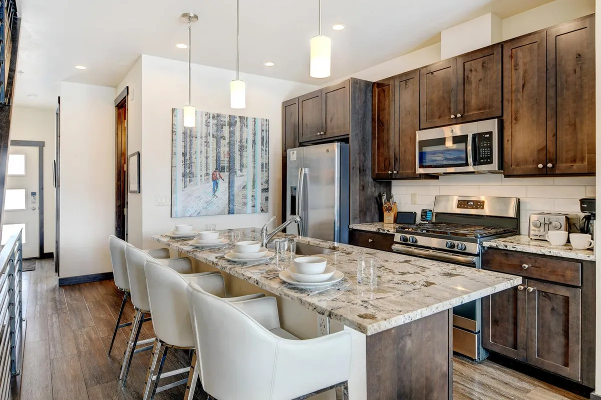 A welcoming, well-lit kitchen showcases a large granite countertop, stainless steel appliances, and spacious layout. There’s a hint of the dining space beyond, inviting group meal preparation and gatherings. The scene captures the energy of cooking and entertaining, from baking sessions to preparing holiday feasts.