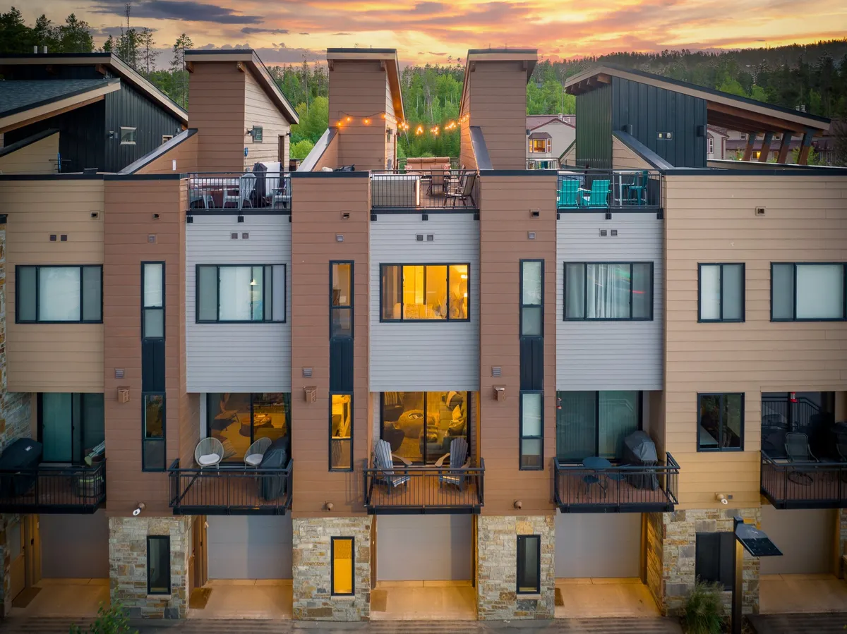 A modern townhome exterior with inviting balconies, each furnished with comfortable seating. Warm lights spill out from the windows, suggesting a cozy, welcoming space inside, while architectural details create a sense of community and shared experience.