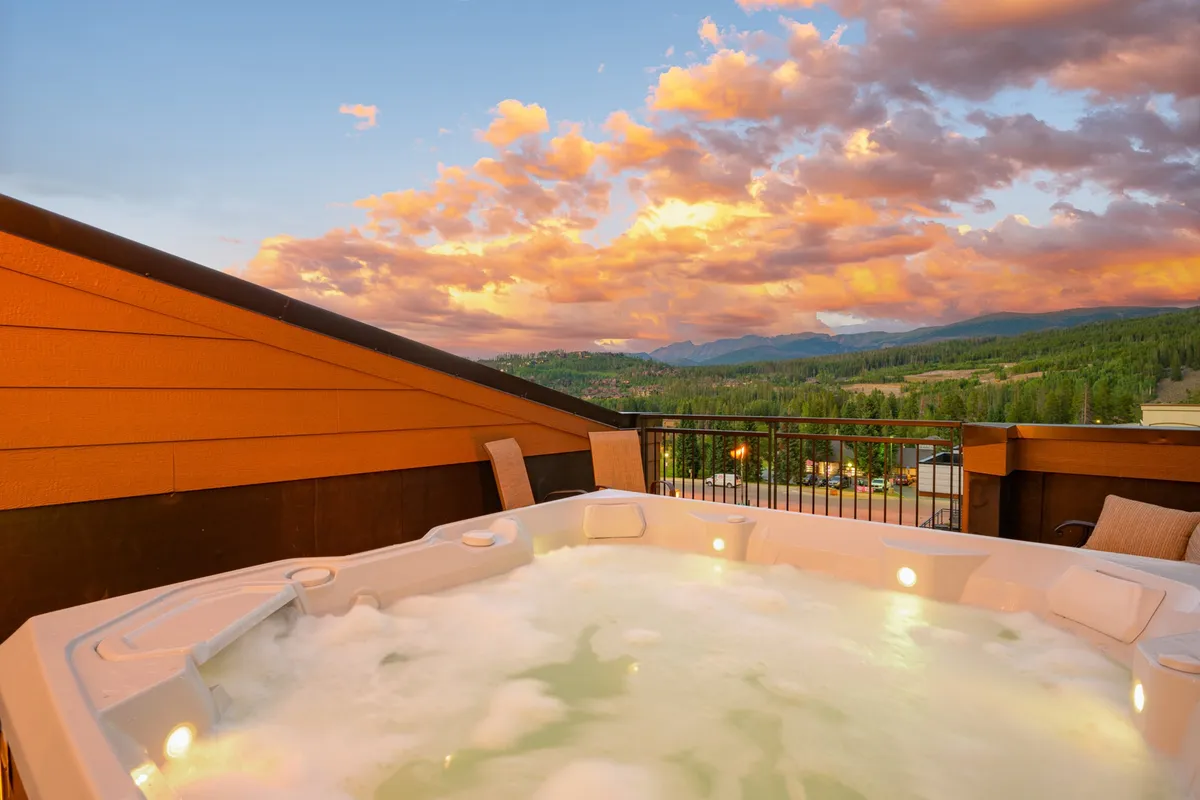 This image captures a private hot tub perched on a deck, overlooking expansive mountain vistas at sunset. The sky is tinged with warm hues, and the scene radiates tranquility and luxury. The deck setting hints at additional outdoor amenities and invites the viewer to imagine relaxing or socializing in this spectacular mountain retreat.