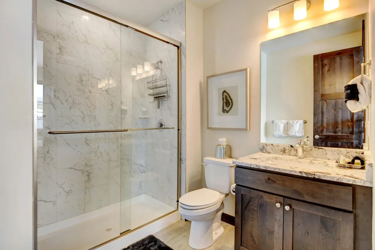 A modern bathroom featuring a glass shower enclosure, marble countertop, wooden cabinetry, and decorative wall art. The space is bright and calming, perfect for relaxing morning routines or winding down with a refreshing shower.