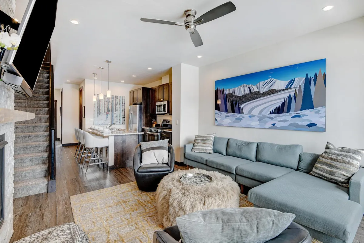 An open-plan living area with a comfortable sofa and coffee table, with the kitchen visible in the background. The arrangement encourages socializing, relaxing, and informal participation in meal prep, blurring the line between cooking and gathering spaces.
