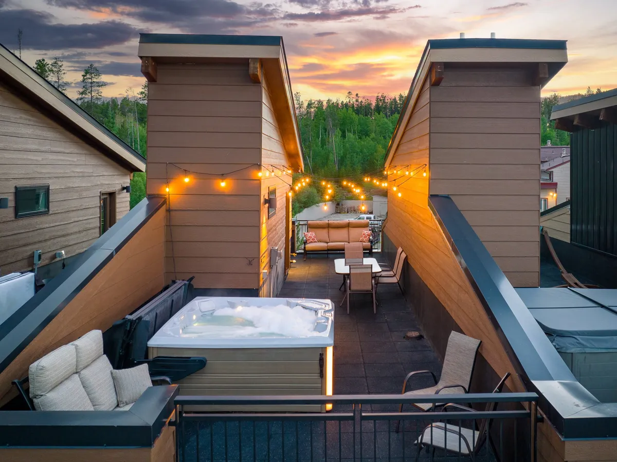 A crisp exterior shot featuring a bubbling hot tub, string lights overhead, and an inviting outdoor seating area. The ambient lighting and comfortable arrangement evoke feelings of warmth, conviviality, and evening gatherings under the Rocky Mountain sky.
